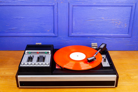 Vintage turntable vinyl record player with red vinyl on table by blue wall.