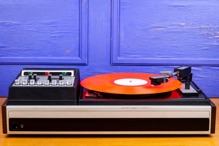 Vintage turntable vinyl record player with red vinyl on table by blue wall.