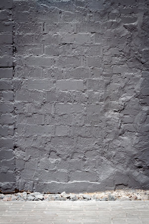 Old weathered wall of bricks painted in black and a sidewalkの写真素材
