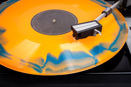 Close up of turntable needle on a vinyl record. Turntable playing vinyl. Needle on rotating orange...