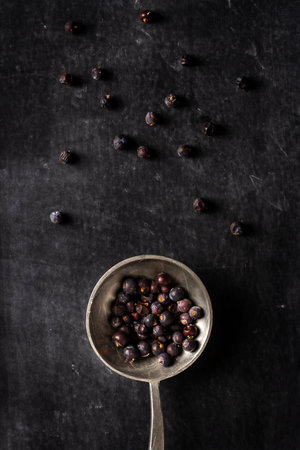 Big old spoon with juniper berries on black background. Flat lay. Top view. Food concept. Dark mood food photography.の写真素材