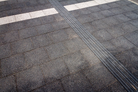 Textured walkway for blind people. Black tactile paving for the visually impaired on the sidewalk.