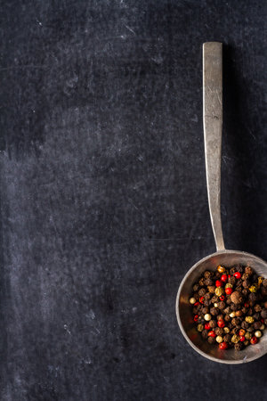 Big old spoon with peppercorn on black background. Flat lay. Top view. Food concept. Dark mood food photography.の写真素材