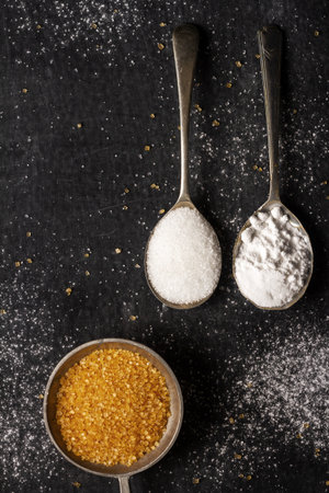 Three old spoons with brown, white and icing sugar on black background. Flat lay. Top view. Food concept. Dark mood food photography.の写真素材