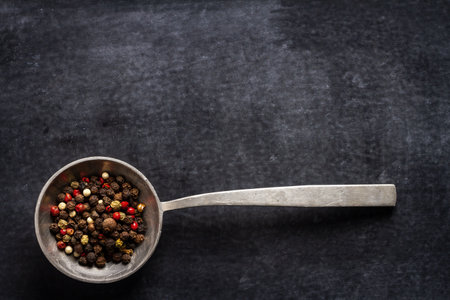 Big old spoon with peppercorn on black background. Flat lay. Top view. Food concept. Dark mood food photography.の写真素材