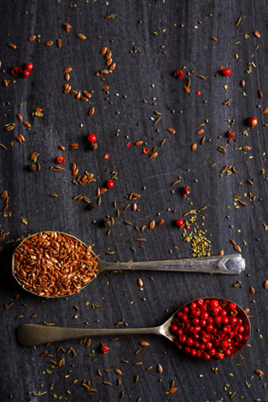 Old spoons with various seeds and spices on black background. Flat lay. Top view. Food concept. Dark mood food photography.の写真素材