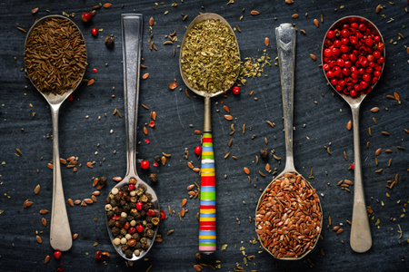 Old spoons with various seeds, herbs and spices on black background. Flat lay. Top view. Food...
