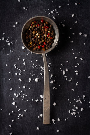 Big old spoon with peppercorn and salt pile on black background. Flat lay. Top view. Food concept. Dark mood food photography.の写真素材