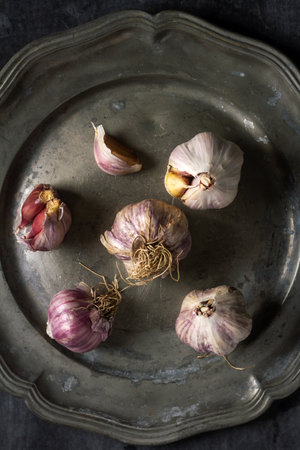 Raw garlic on grey pewter plate. Flat lay. Top view. Food concept. Dark mood food photography.