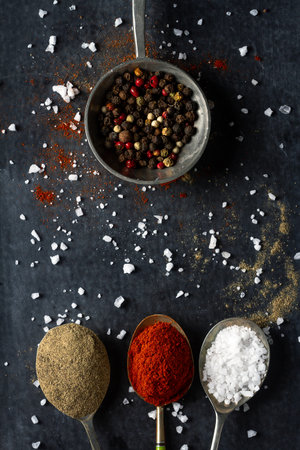 Old metal spoons with different kind of spices on black background. Flat lay. Top view. Food concept. Dark mood food photography.の写真素材