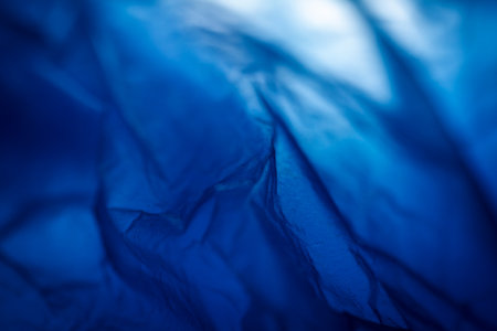 Extreme close up of blue empty plastic bag background. The plastic surface is wrinkly and tattered making abstract pattern. Selective focus, shallow depth of field.の写真素材