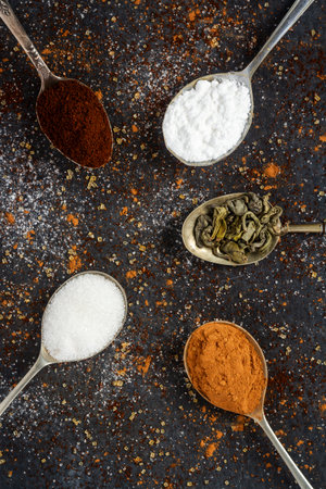 Spoons with icing sugar, coffee and cocoa on black background sprinkled with brown and white sugar.の写真素材