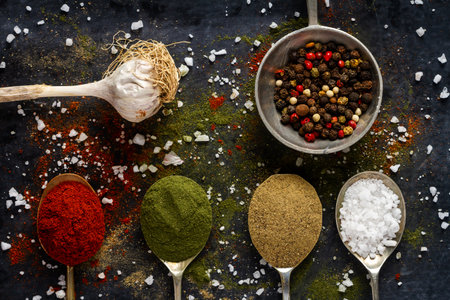 Old metal spoons with different kind of spices on black background. Flat lay. Top view. Food...