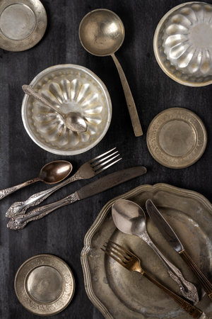 Vintage pewter plates, bowls and cutlery on black chalkboard background. Flat lay. Top view. Food concept. Dark mood food photography.の写真素材