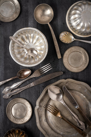 Vintage pewter plates, bowls and cutlery on black chalkboard background. Flat lay. Top view. Food concept. Dark mood food photography.の写真素材