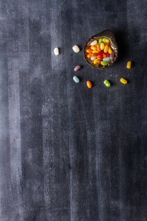Small metal bowl of colorful sweet jellybeans on black chalkboard background. Flat lay. Top view....