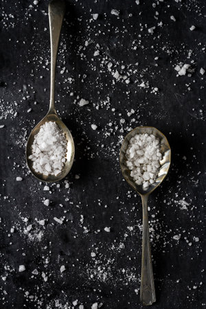 Top view of a spoons with coarse grained sea salt on black background. Flat lay. Top view. Food concept.の写真素材