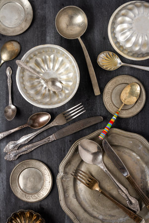 Vintage pewter plates, bowls and cutlery on black chalkboard background. Flat lay. Top view. Food concept. Dark mood food photography.の写真素材