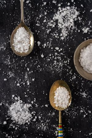 Top view of a spoons with coarse grained sea salt on black background. Flat lay. Top view. Food concept.の写真素材