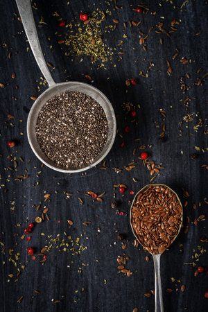 Old spoons with chia and flax seeds on black background. Flat lay. Top view. Food concept. Dark mood food photography.の写真素材