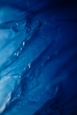 Extreme close up of blue empty plastic bag background. The plastic surface is wrinkly and tattered making abstract pattern. Selective focus, shallow depth of field.の写真素材
