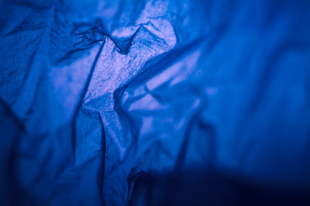 Extreme close up of blue empty plastic bag background. The plastic surface is wrinkly and tattered making abstract pattern. Selective focus, shallow depth of field.の写真素材