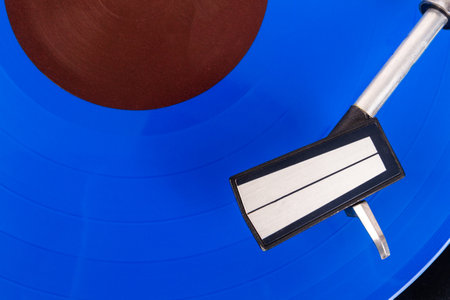 Close up of turntable needle on a vinyl record. Turntable playing vinyl. Needle on rotating blue...