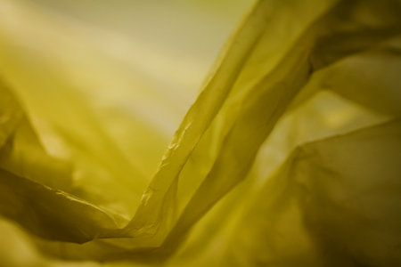 Extreme close up of yellow empty plastic bag background. The plastic surface is wrinkly and tattered making abstract pattern. Selective focus, shallow depth of field.の写真素材