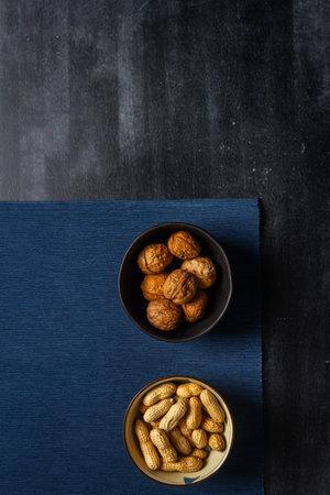 Two bowls with nuts and blue table cloth on black chalkboard background. Flat lay. Top view.の写真素材