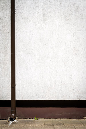 White stucco concrete grunge wall with brown drain pipe and a sidewalk
