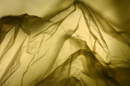 Extreme close up of yellow empty plastic bag background. The plastic surface is wrinkly and tattered making abstract pattern. Selective focus, shallow depth of field.の写真素材