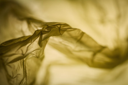 Extreme close up of yellow empty plastic bag background. The plastic surface is wrinkly and tattered making abstract pattern. Selective focus, shallow depth of field.の写真素材