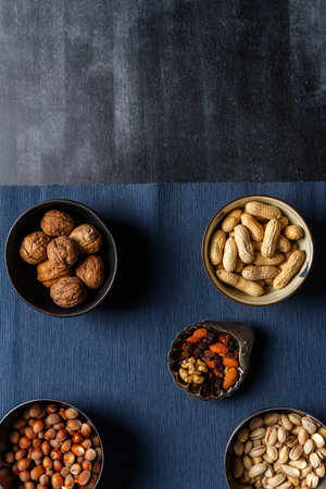 Bowls with nuts and blue table cloth on black chalkboard background. Flat lay. Top view.