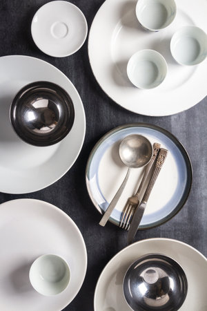Top view of an empty plates, bowls, glasses and cutlery placed on a black chalkboard background....