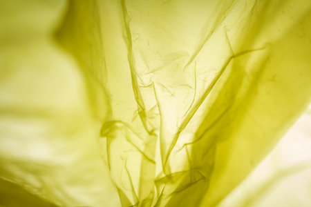 Extreme close up of yellow empty plastic bag background. The plastic surface is wrinkly and tattered...