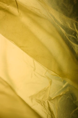 Extreme close up of yellow empty plastic bag background. The plastic surface is wrinkly and tattered...