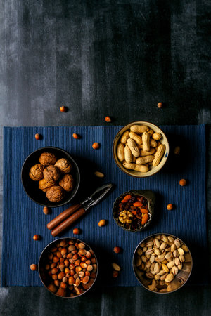 Bowls with nuts and blue table cloth on black chalkboard background. Flat lay. Top view.