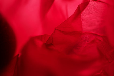 Extreme close up of red empty plastic bag background. The plastic surface is wrinkly and tattered making abstract pattern. Selective focus, shallow depth of field.の写真素材