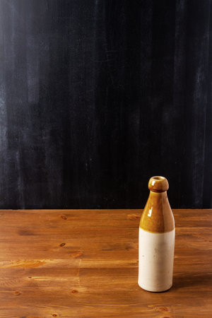 Old stoneware bottle on brown wooden table by the black wall. Still life.の写真素材