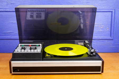 Vintage turntable vinyl record player with yellow vinyl on a tableの写真素材