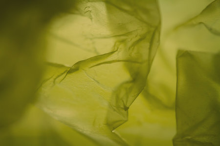 Extreme close up of yellow empty plastic bag background. The plastic surface is wrinkly and tattered making abstract pattern. Selective focus, shallow depth of field.の写真素材