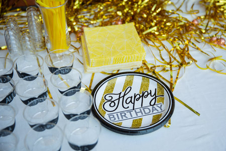 Happy birthday party with champagne glasses and golden plates on white table.の写真素材