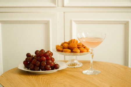A glass of pink wine and a plate of grapes on a wooden tableの写真素材