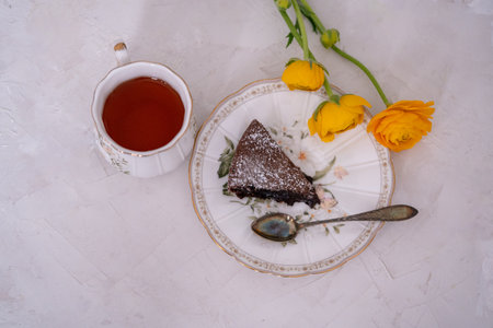 Chocolate cake on a plate with a cup of tea and yellow buttercupsの写真素材