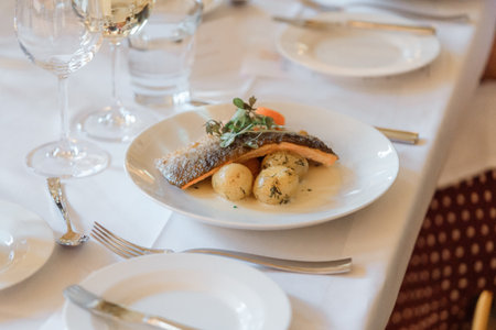 Fish fillet with potatoes and herbs on a white plate in a restaurantの写真素材