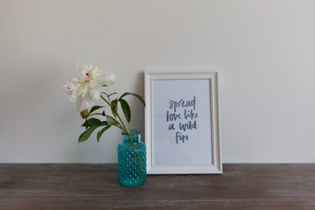 White peony in a blue vase and white frame on a wooden table