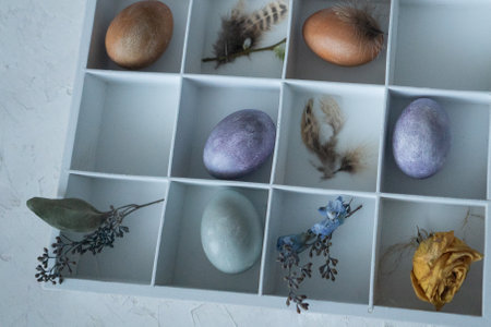 Easter eggs in a white box with feathers and dried flowers.