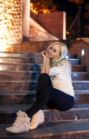girl in leggins and sneakers are sitting on the stairs in the eveningの写真素材