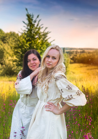 Two ukrainian girls in national costumes at the evening flower meadowの写真素材