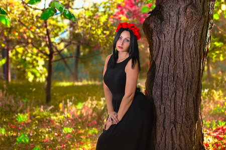 Black haired gothic woman in the chaplet of red flowers at the colorfull nature backgroundの写真素材
